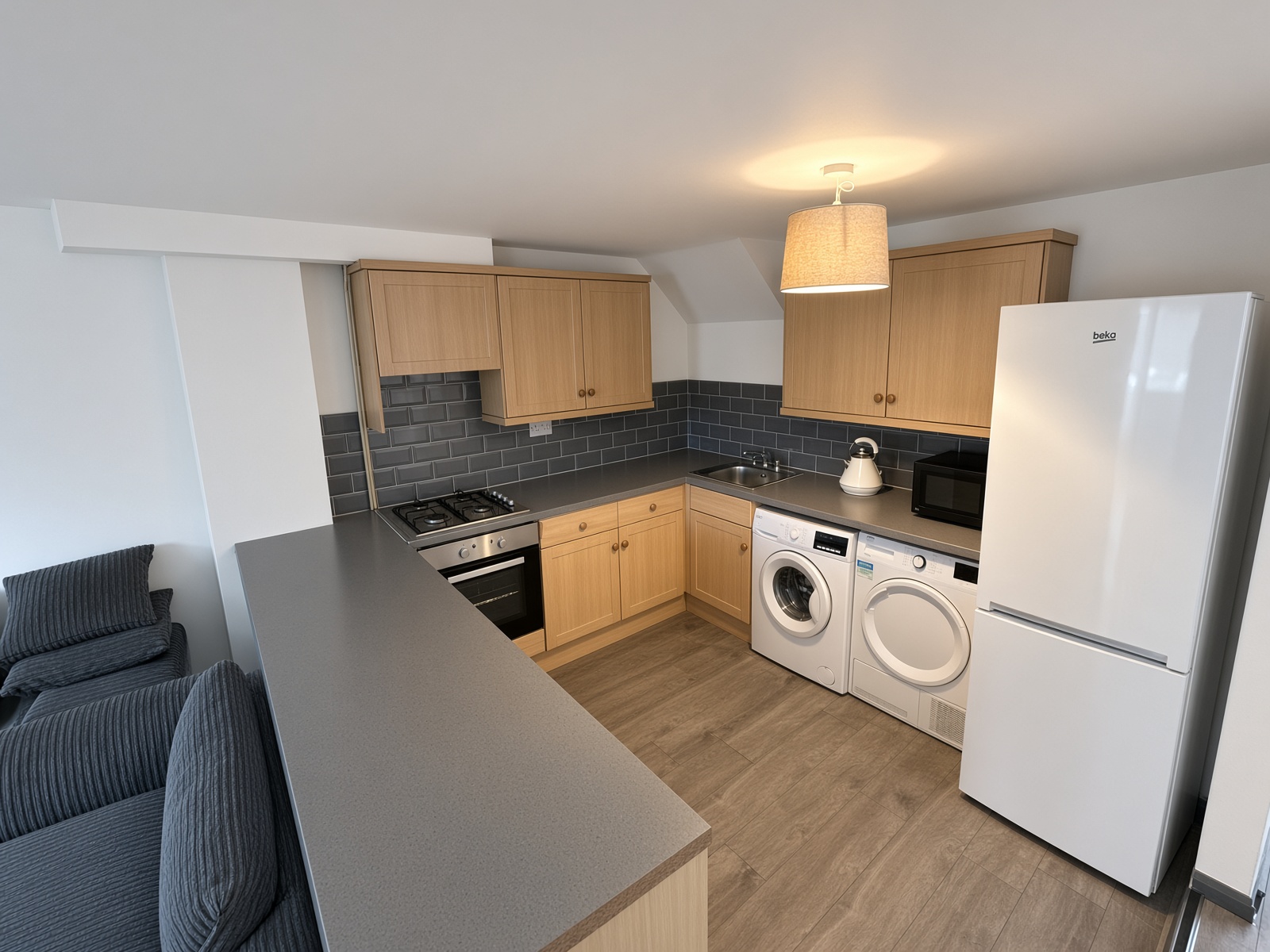 Kitchen with light wood cabinets, grey worktop, hob, oven, washer and dryer