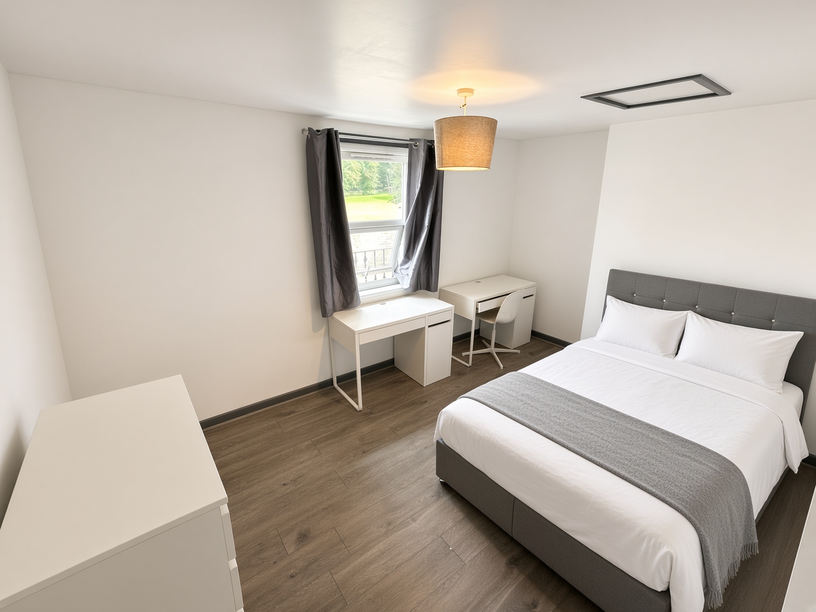 Bedroom with grey headboard, twin white desks under the window, and wood-effect floor