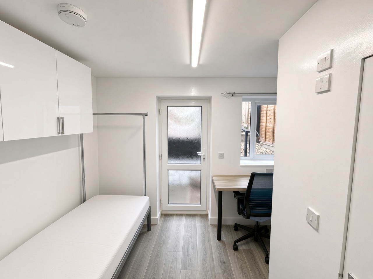 Bedroom with a metal clothes rail, a glass-panelled door, and a desk in the corner