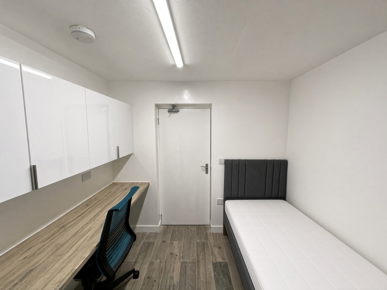 Bedroom with a grey headboard, white overhead cabinets, and a blue office chair