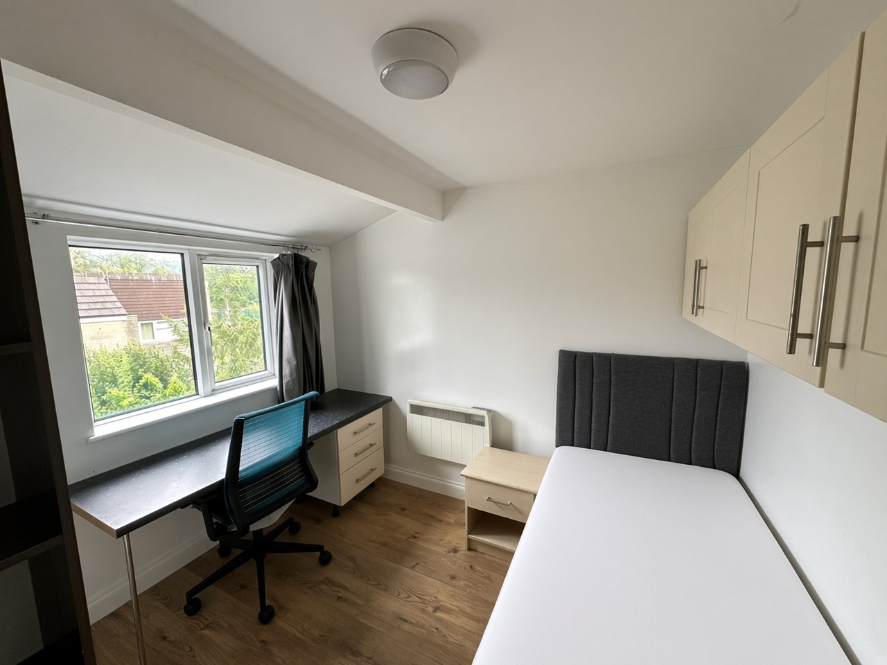Bedroom with a grey headboard, light-wood nightstand, and a desk under the window
