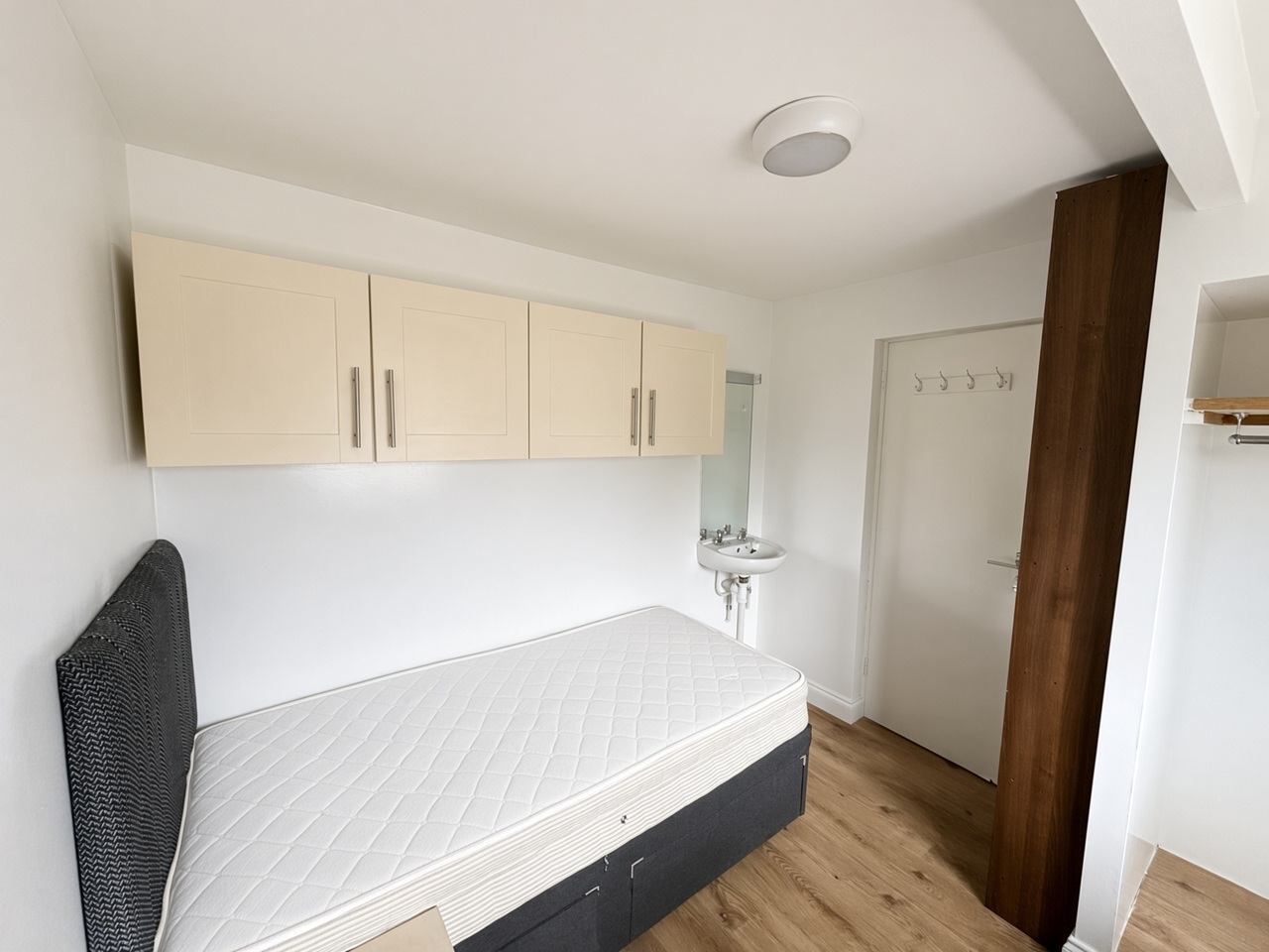 Bedroom with a wall-mounted sink, cream overhead cabinets, and a grey headboard
