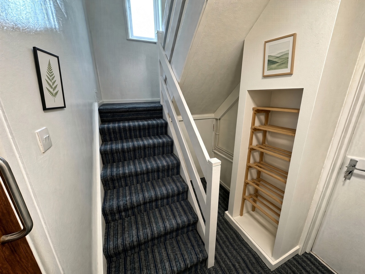 Hallway staircase with blue striped carpet, a white banister, and a shoe rack in the alcove