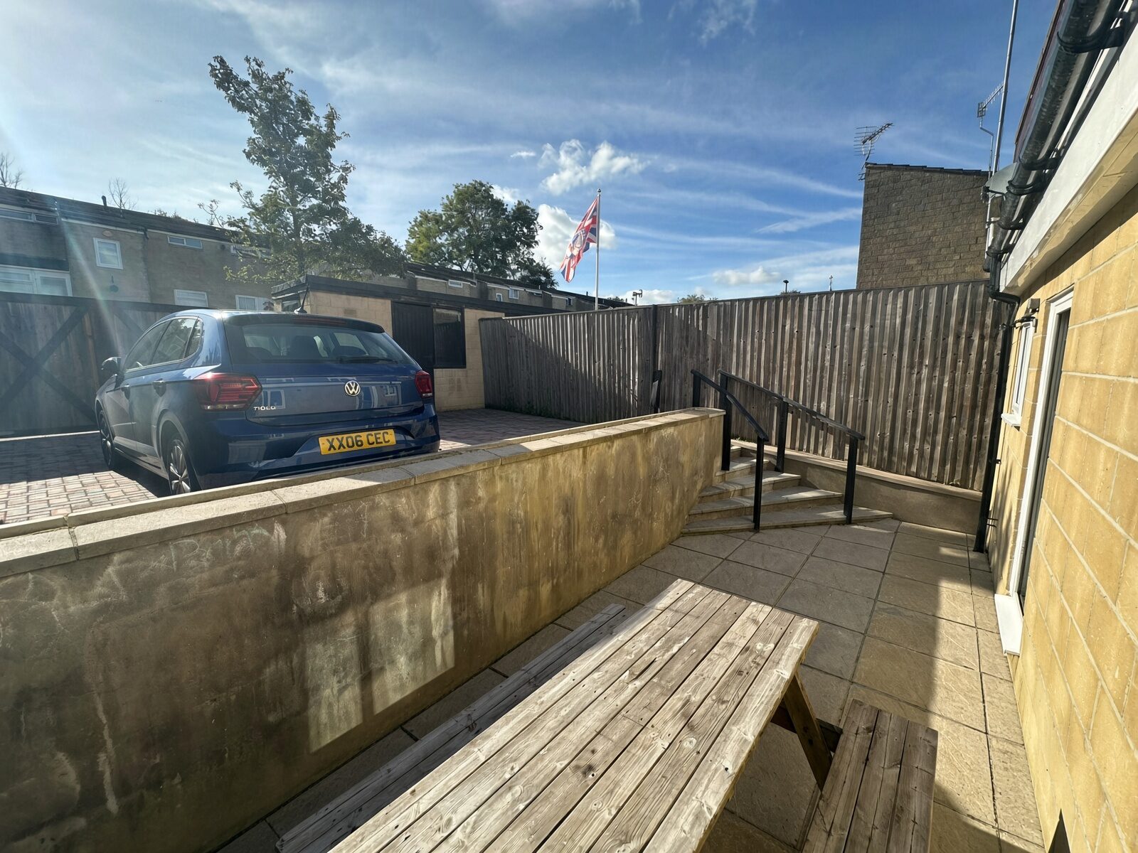 Garden with patio seating, fencing and parking area beyond