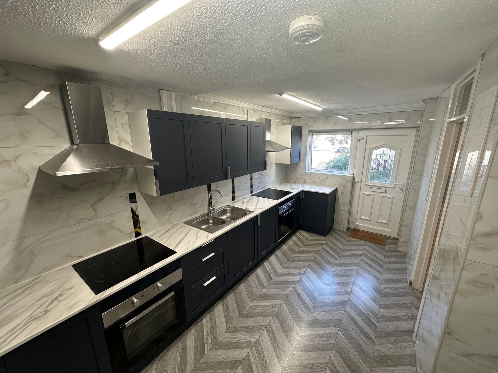 Kitchen with dark units, marble-effect worktops and extractor hood