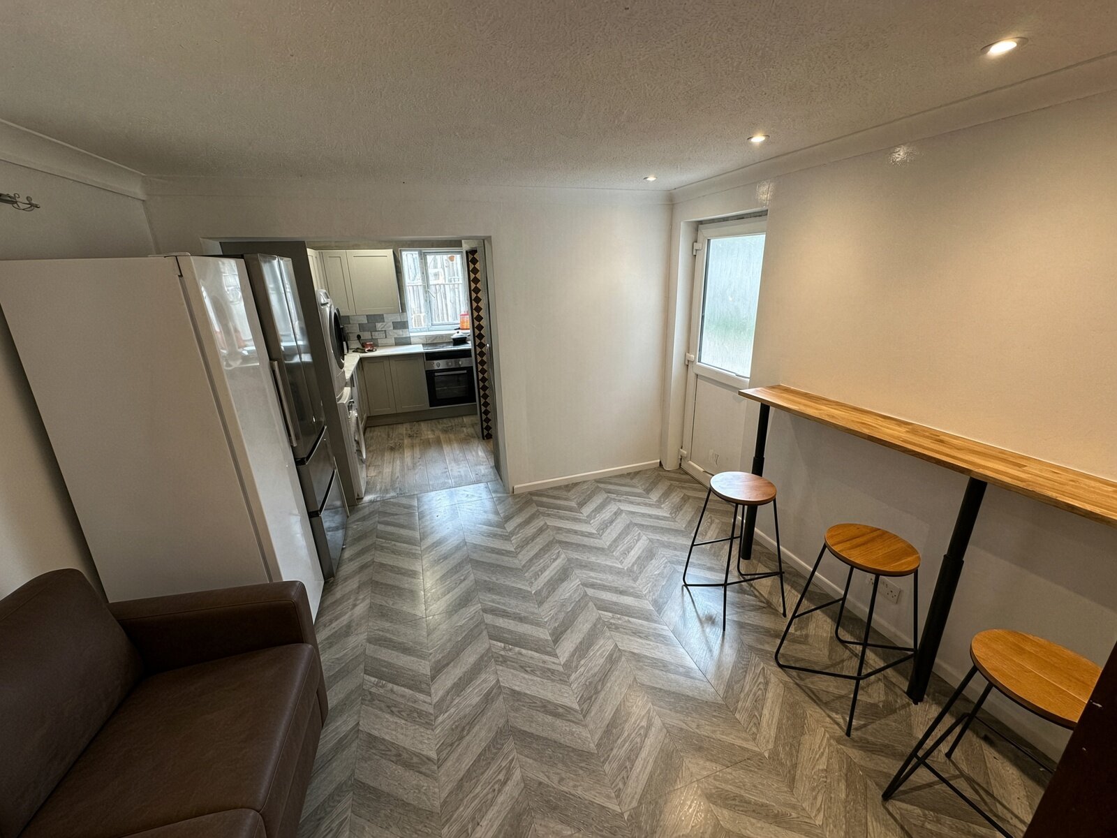 Open-plan living and dining room with breakfast bar, stools and herringbone floor