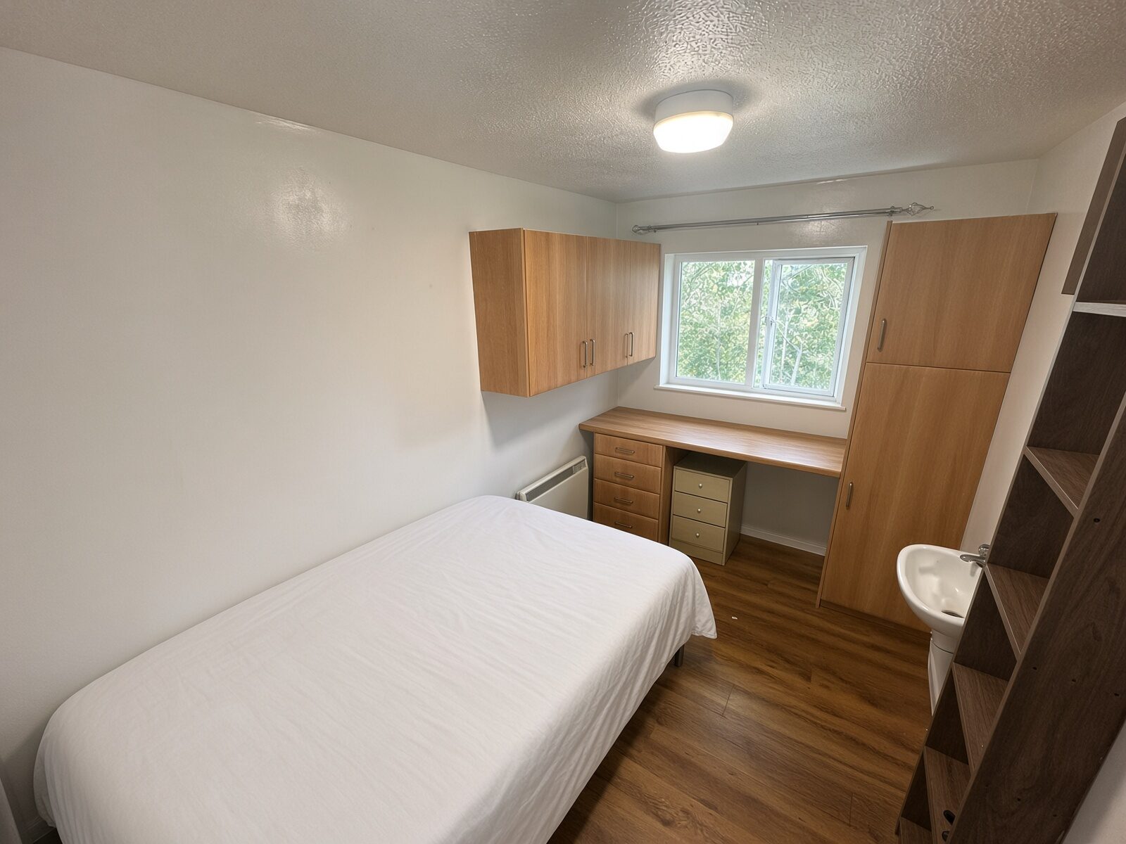 Bedroom with single bed, wood desk, overhead cupboards and window