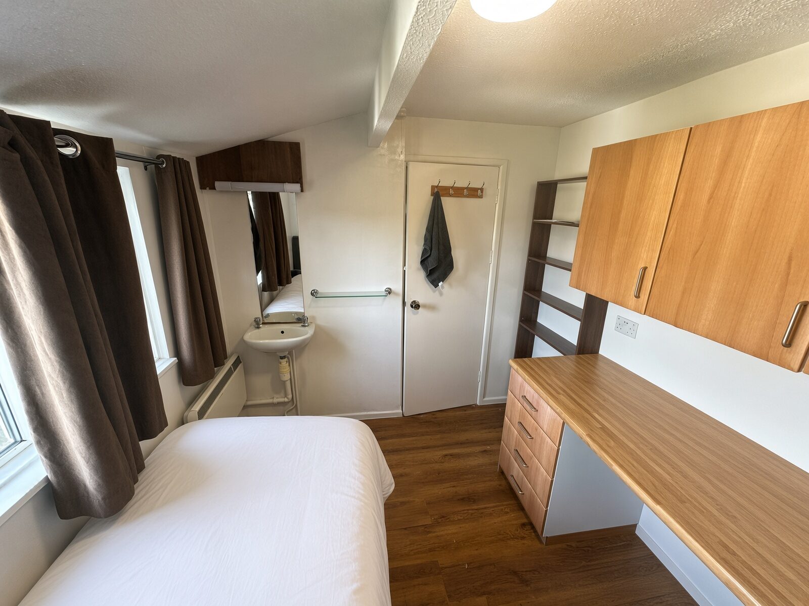 Bedroom with single bed, wood desk, overhead cupboards and basin