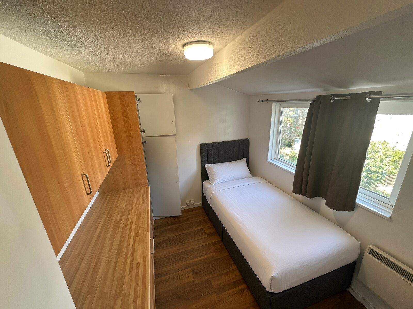Bedroom with single bed, wood desk and overhead cupboards by the window