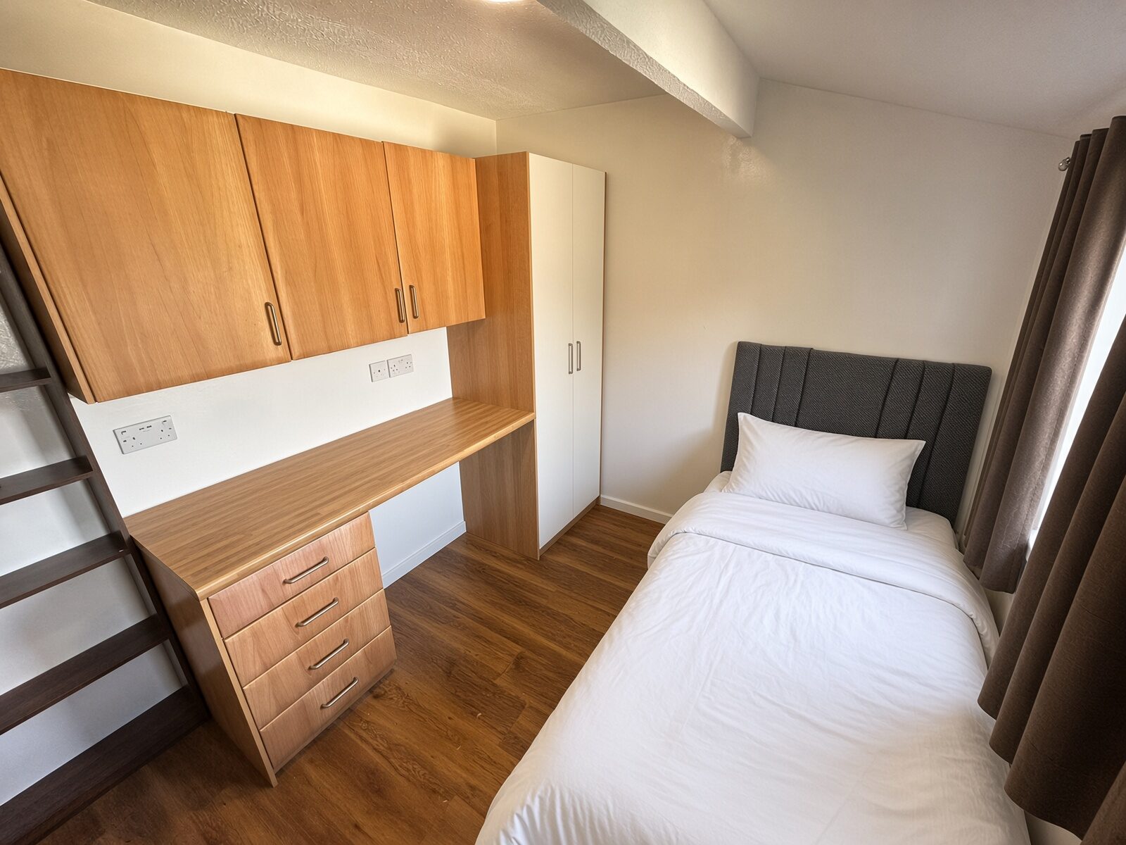 Bedroom with single bed, wood desk and overhead cupboards