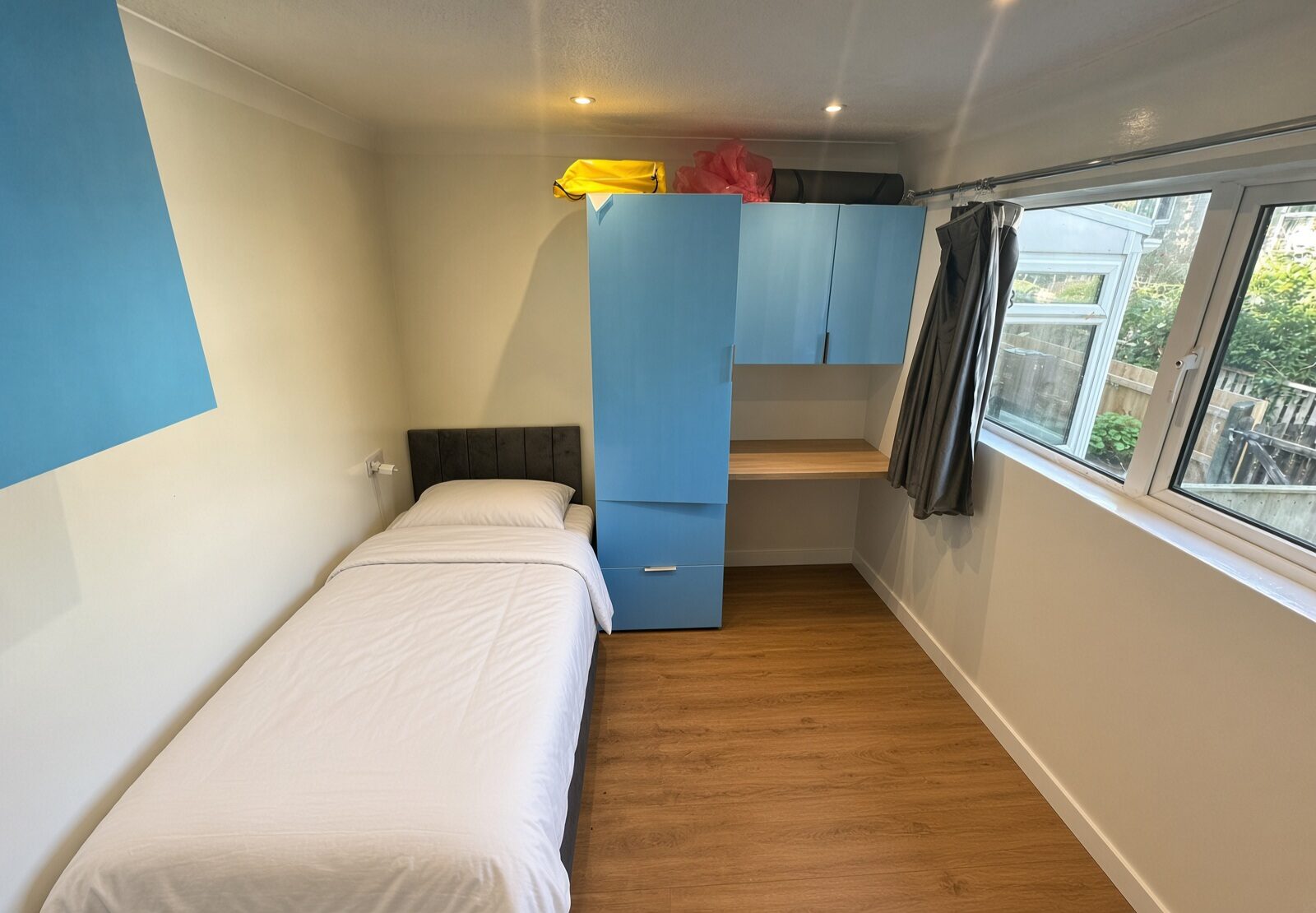 Bedroom with single bed, blue wardrobe, desk and large window