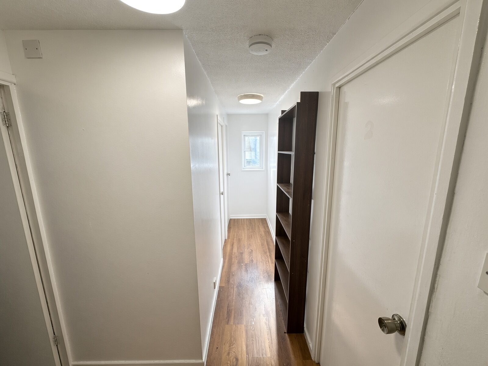 Hallway with wood floor, shelving and bedroom doors
