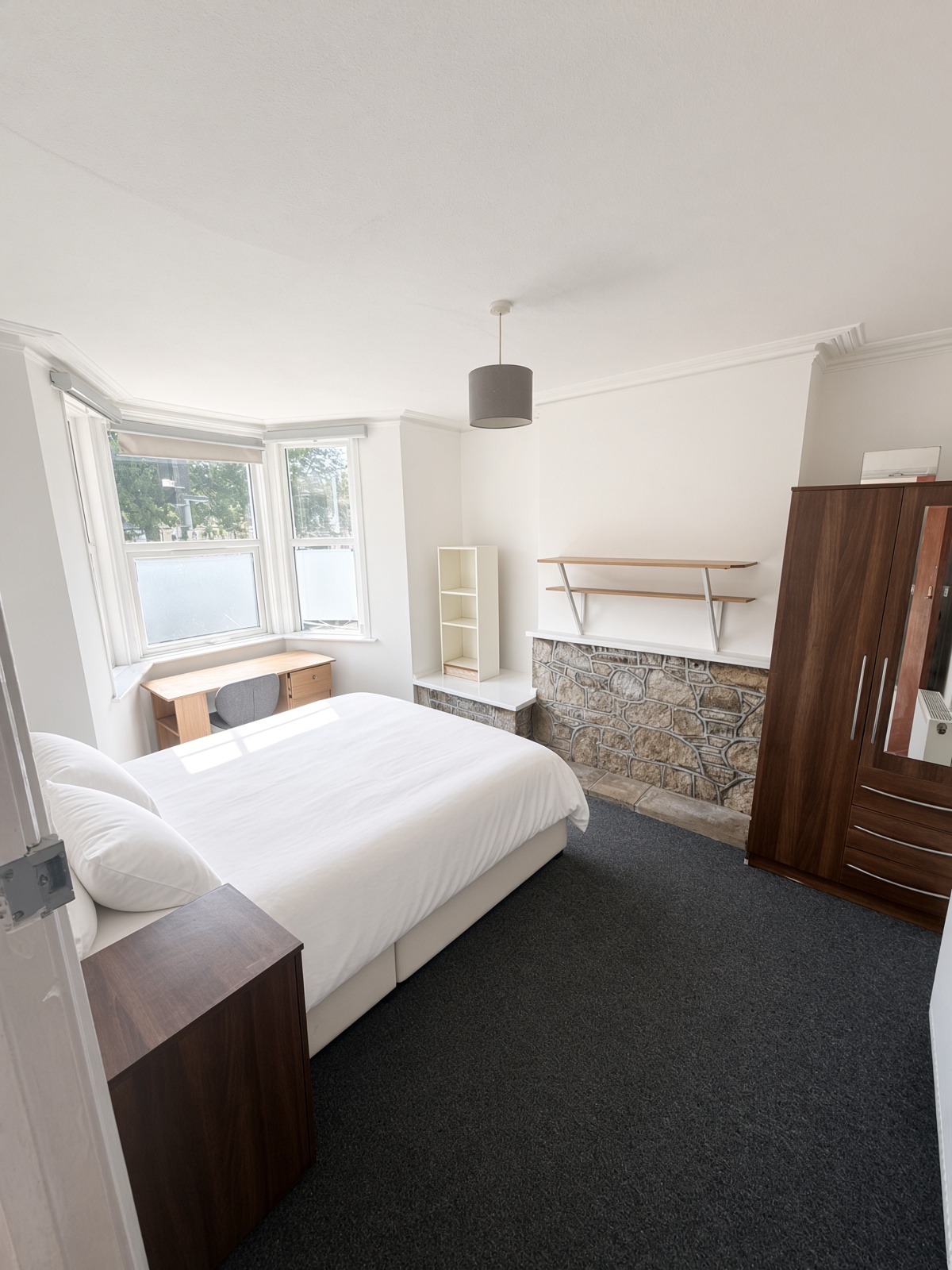 Bedroom with a stone chimney-breast, white bed, and bay-window desk
