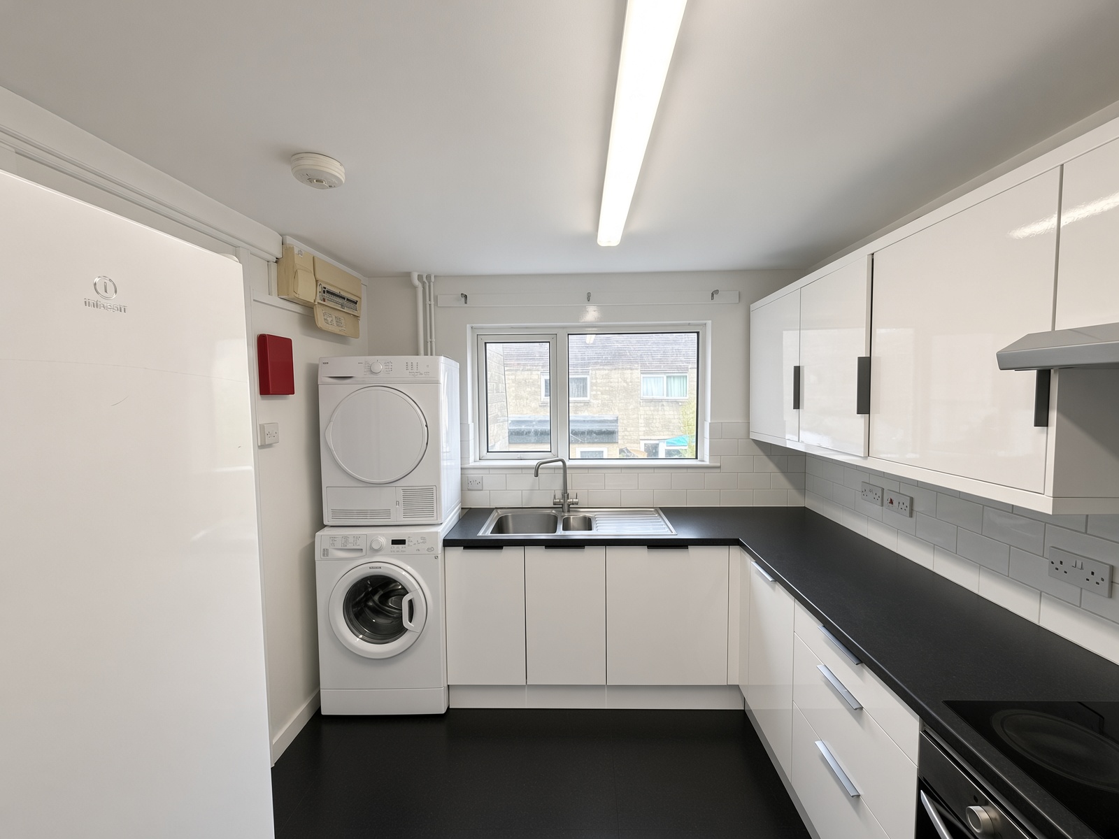 Kitchen with white cabinets, a black worktop, a fridge, and a washer-dryer stack