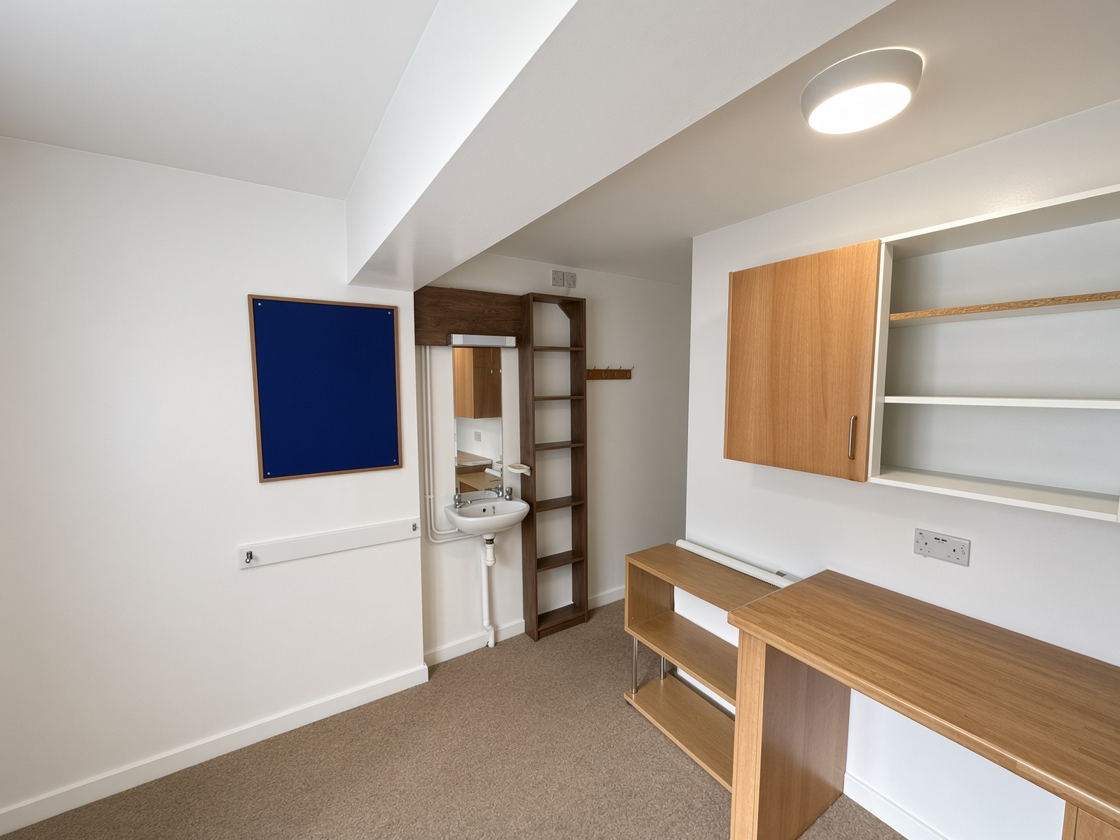 Bedroom study with a built-in desk, a washbasin, and a blue notice board