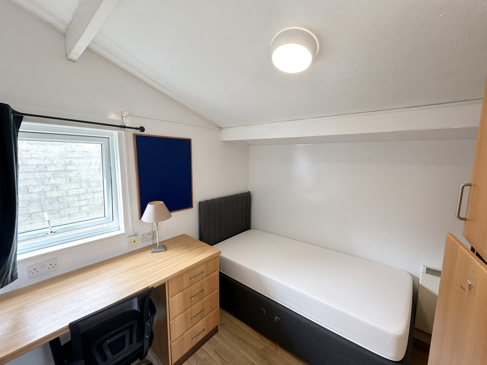 Top-floor bedroom with a built-in desk, a grey headboard, and a blue pinboard