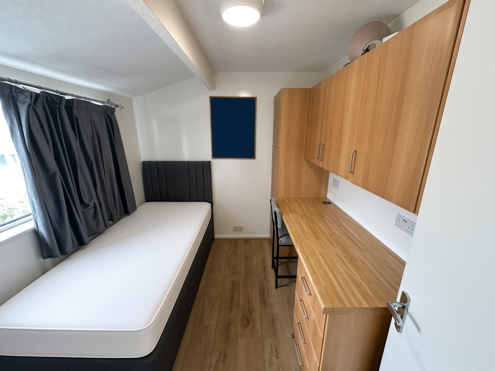 Bedroom with a grey single bed and a built-in desk and wardrobe