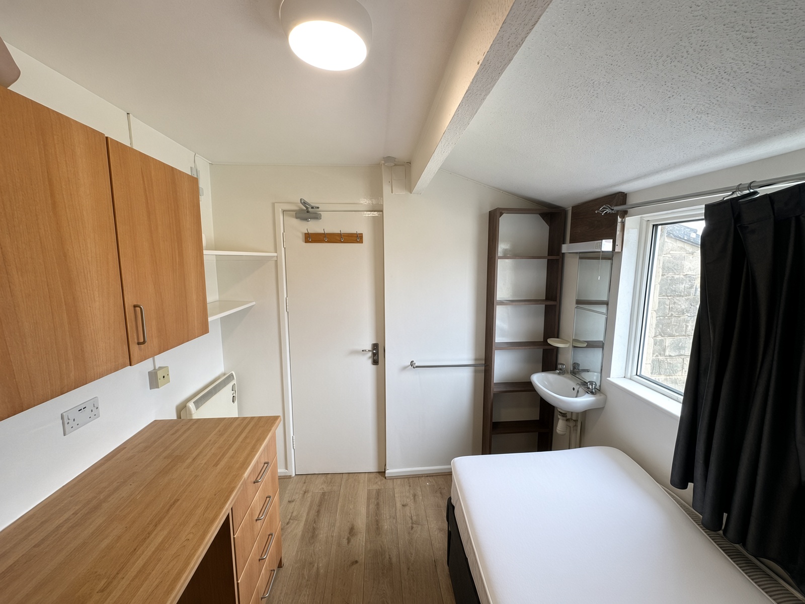 Bedroom with a built-in desk, a washbasin, and a dark open shelving unit