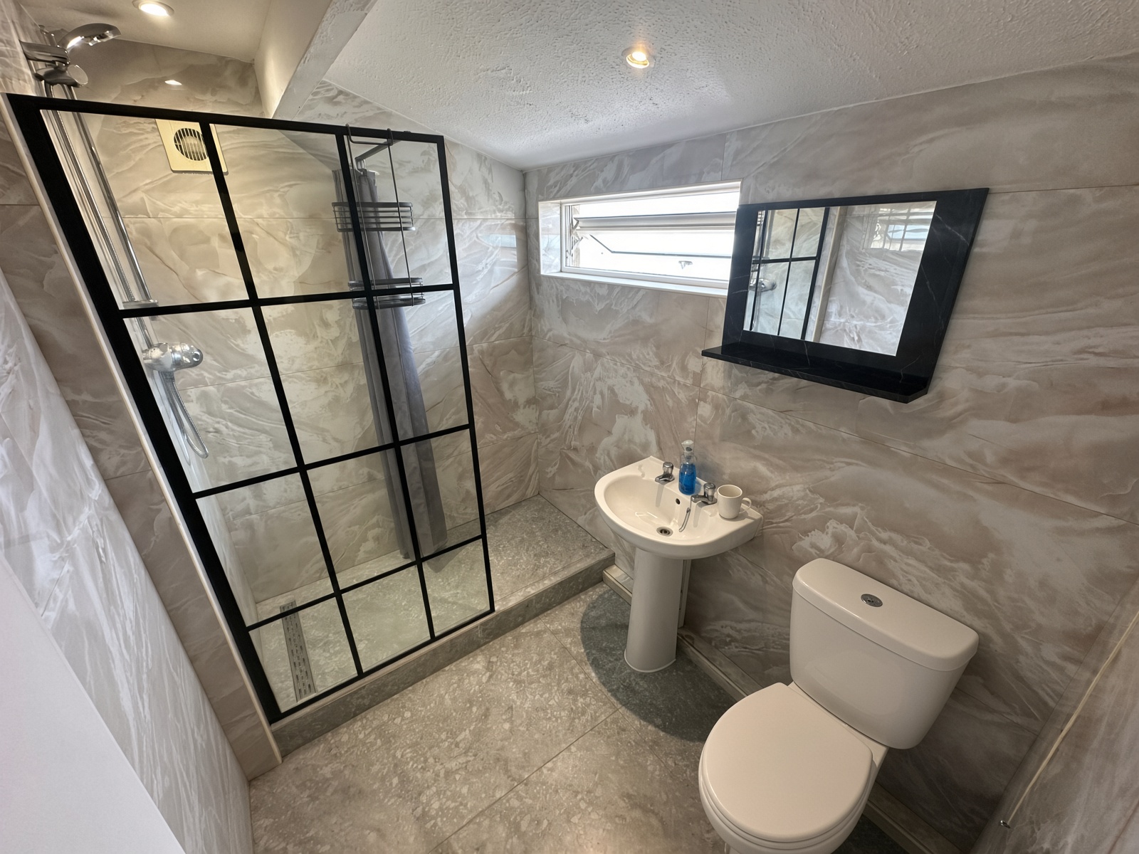 Bathroom with marble-effect tiles, a black-framed shower screen, and a black-framed mirror