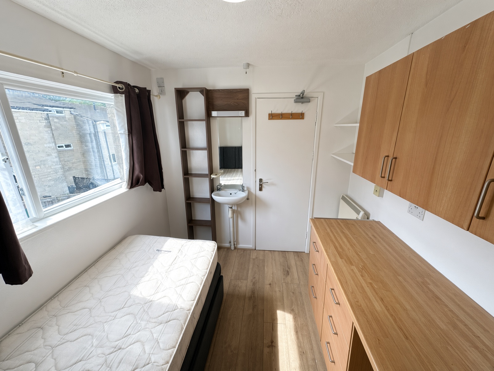 Bedroom with a bed under the window, a washbasin, and light-wood storage