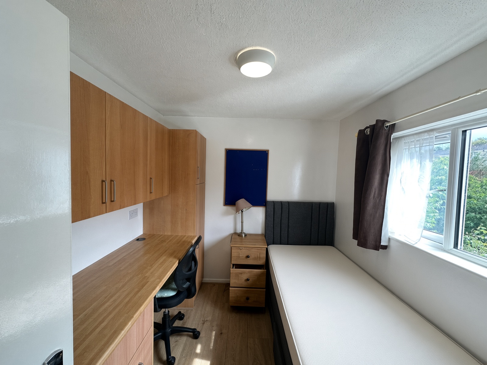 Bedroom with a built-in desk, a grey headboard, and brown curtains
