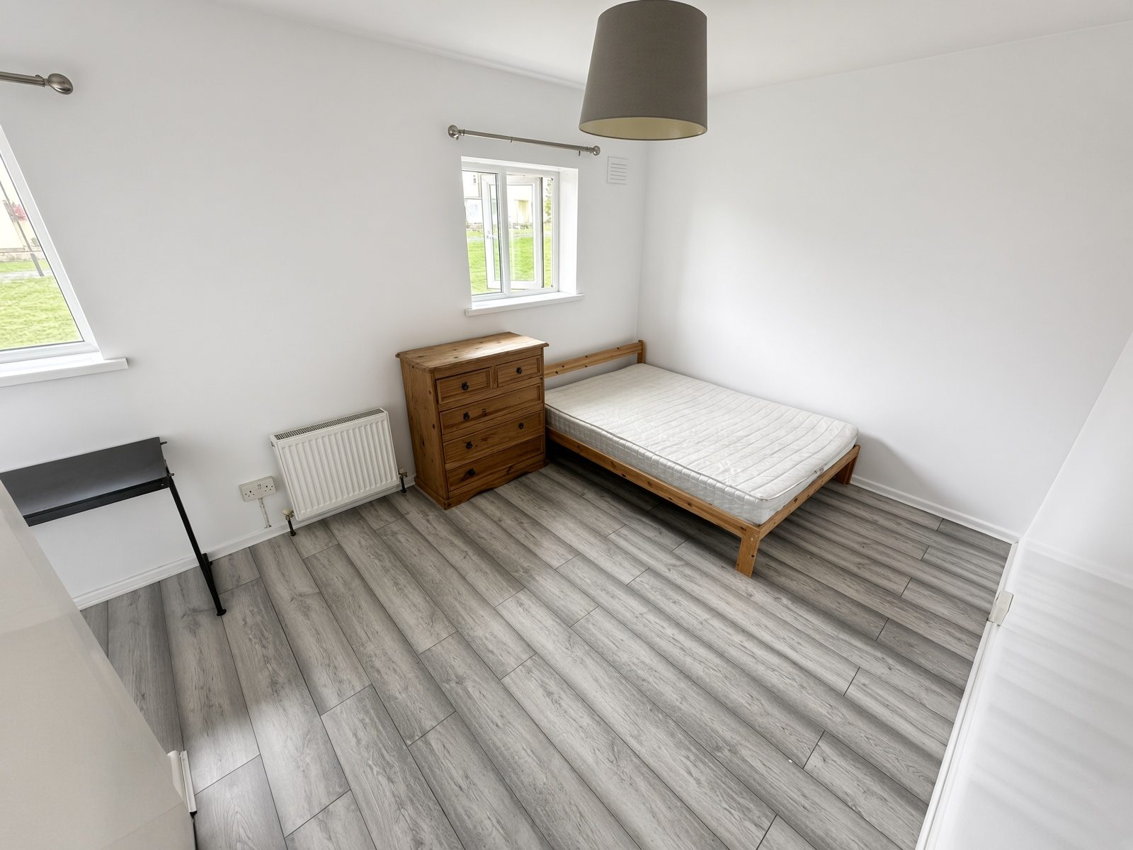 Bedroom with a pine bed and chest of drawers, and two windows over the grass