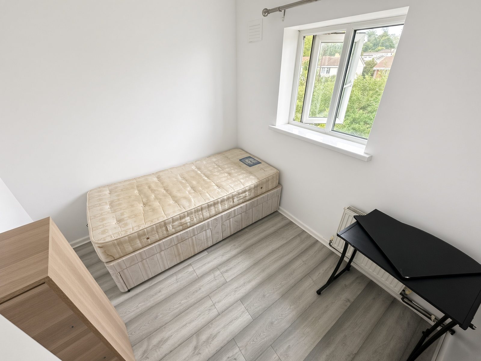 Narrower bedroom with a single mattress, black desk, and window