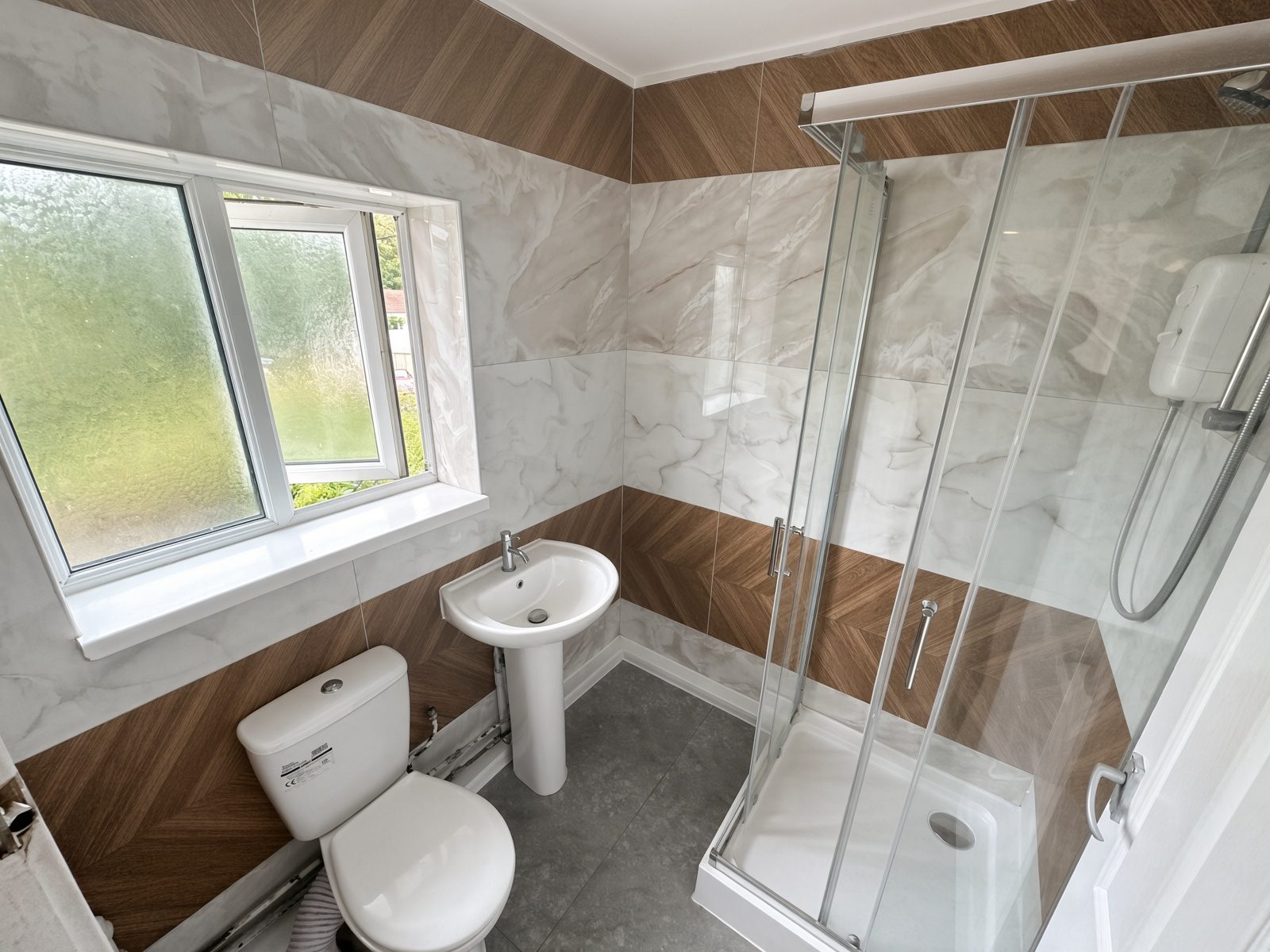 Shower room with marble and wood-effect tiles, a glass cubicle, basin, and toilet